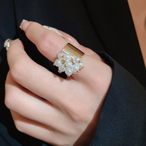 Detailed close-up of a wide golden ring with white pearls against a dark suit background