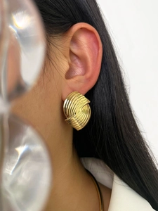 Detailed view of geometric gold metal earrings with unique texture on model ear