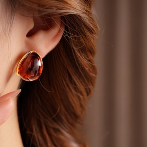 Close-up of amber resin round stud earrings with gold trim worn by a model