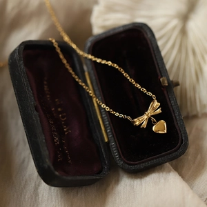 Elegant 18K gold plated titanium necklace with bow and heart pendants on a jewelry box