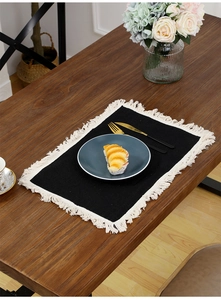 Detail of black rectangular cotton linen placemat with white woven tassels on wood table