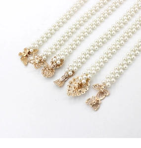 Détail de cinq ceintures en perles blanches avec diverses boucles dorées sur fond blanc