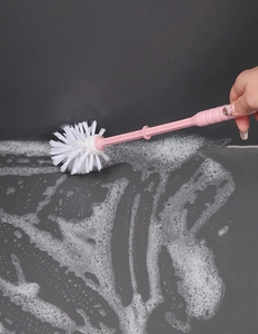 Pink toilet brush cleaning a grey tile floor with white soap foam detail shot