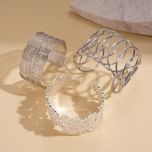 Three silver geometric open cuff bracelets featuring floral cutout and spiral metal designs