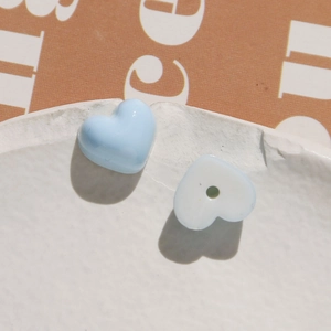 Macro shot of two light blue heart-shaped resin beads on a textured white ceramic plate