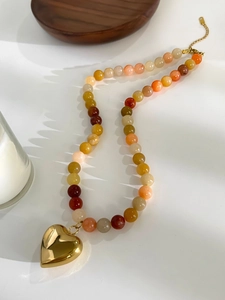 Detail of heart pendant necklace featuring warm-toned natural stone beads and gold hardware