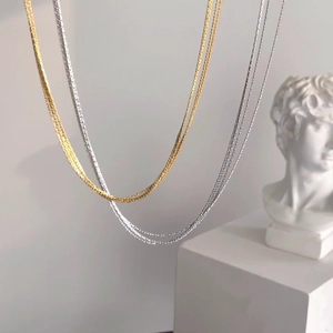 Layered gold and silver snake chain necklaces in titanium steel displayed on a pedestal