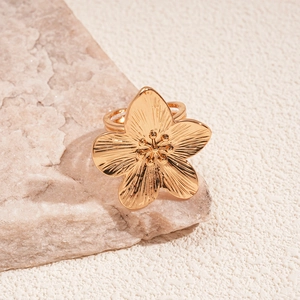 Detailed close-up of golden flower ring with textured petals on a natural stone surface