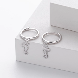 Macro shot of silver seahorse dangle earrings on white minimalist geometric stand