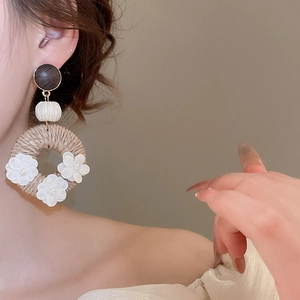 Detail of bohemian rattan drop earring with fabric flowers and pearls on a model
