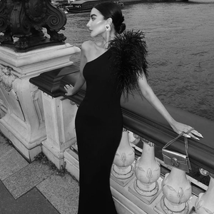 Detail of elegant black one-shoulder evening gown featuring feather accents on shoulder