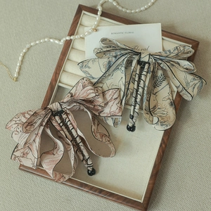 Detail of floral ink-wash bow hair clips on a vintage wooden tray with pearl accents