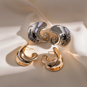 Detail von C-förmigen Metallohrsteckern in Gold und Silber auf edlem Seidenstoff