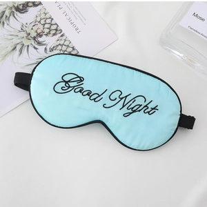 Flat lay of a light blue silk sleep mask with black Good Night embroidery on white fabric