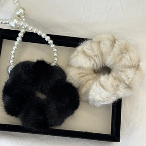Close-up of black and beige plush faux fur scrunchies with soft texture on a display tray