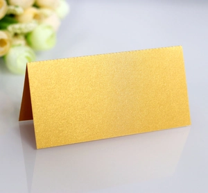Close-up of golden pearlescent paper fold tent card with reflection on white surface