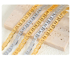 Detail of interlocking gold and silver mariner link necklaces on travertine stone surface
