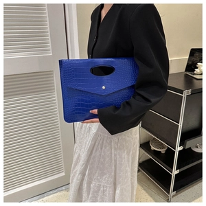 Detail of blue crocodile pattern envelope clutch bag with oval handle and metal stud