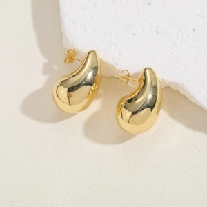 Detail view of gold-plated teardrop earrings with mirror-polished finish on white stone