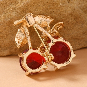 Macro shot of a gold cherry brooch with red faceted gems and crystals on a stone