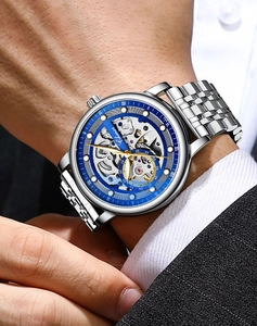 Macro detail of men's automatic skeleton watch with silver band and blue bezel on wrist