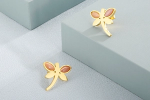 Detailed macro view of golden dragonfly stud earrings with pink gemstone on grey steps