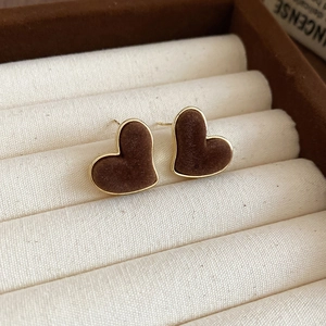 Close-up of brown velvet heart studs with gold edges in a beige jewelry box