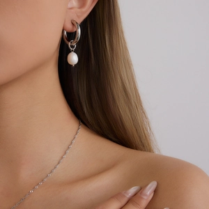 Close-up of silver stainless steel hoop earring with irregular pearl on a model