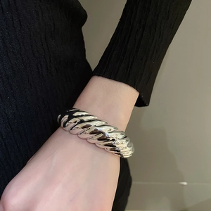 Close-up of a chunky silver croissant twist cuff bracelet on a woman's wrist