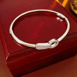 Detailed close-up of a silver-tone zircon buckle bangle on a red wooden surface
