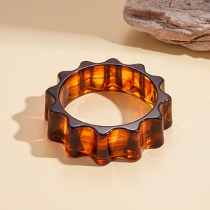 Close-up of a wide amber resin bangle with gear-shaped edges on a stone background