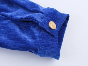 Dettaglio della trama in ciniglia blu reale e bottone metallico dorato sul polsino