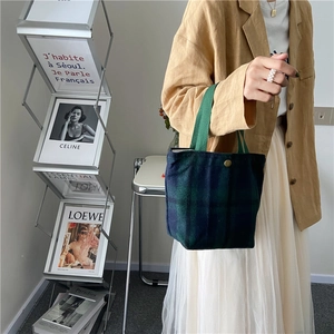 Detail of wool-like plaid handbag featuring a green fabric strap and golden buckle