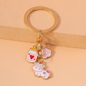 Cartoon enamel cow and pink cloud keychain with gold-tone hardware on warm background