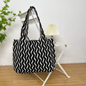Chic black and white wavy knit tote bag hanging on a chair in a cozy home interior setting