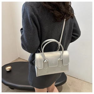 Detail of silver metallic handbag with top handles and shoulder strap on model