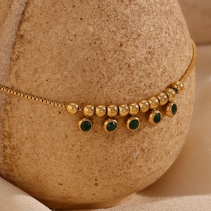 Detail view of gold stainless steel anklet with green gemstone pendants on display