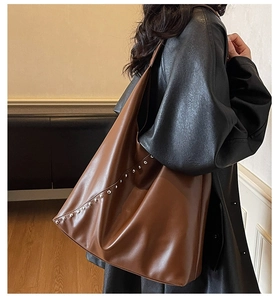 Close-up of a large dark brown PU leather tote bag with silver studs and flat strap
