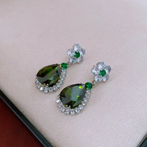 Detailed macro of silver-tone flower earrings with pear-cut deep green zircon drops