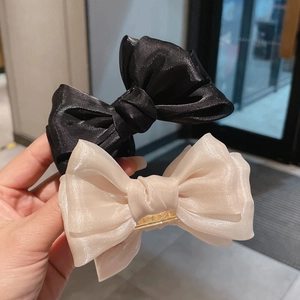 Detail showing the glossy silk fabric texture and large double-layer bow on hair clip