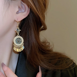 Detail of bohemian gold tassel earrings with dark gemstone and faux pearl accents
