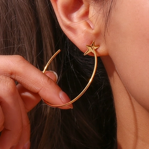 Close-up of golden stainless steel star stud earrings with a large thin hoop on a model