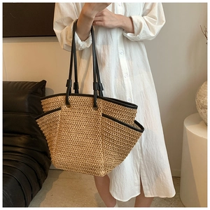 Detailed view of straw woven tote bag featuring black faux leather straps and trim