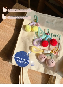 Detail of plush cherry bag charms with embroidered expressions on a canvas tote bag
