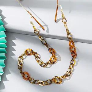 Detail of tortoise shell acrylic eyeglass chain with gold accents on a stone surface