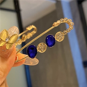 Close-up of golden safety pin brooch with blue gemstones and white crystals