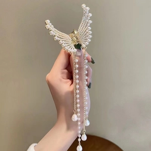 Close-up of golden butterfly hair claw clip with white faux pearls and long tassel pendant