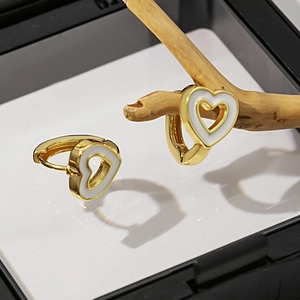 Vue macro de boucles d'oreilles cœur dorées avec émail blanc et motif géométrique