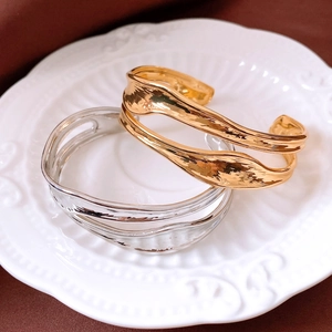Dettaglio di bracciali aperti in oro e argento con texture lavica su un piatto di porcellana