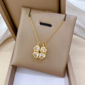 Golden clover necklace with heart-shaped crystal pendant on a soft jewelry pillow